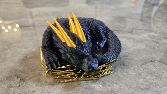 3D printed sleeping dragon in silk blue with gold horns curled in a black nest-shaped base used as a paper clip holder