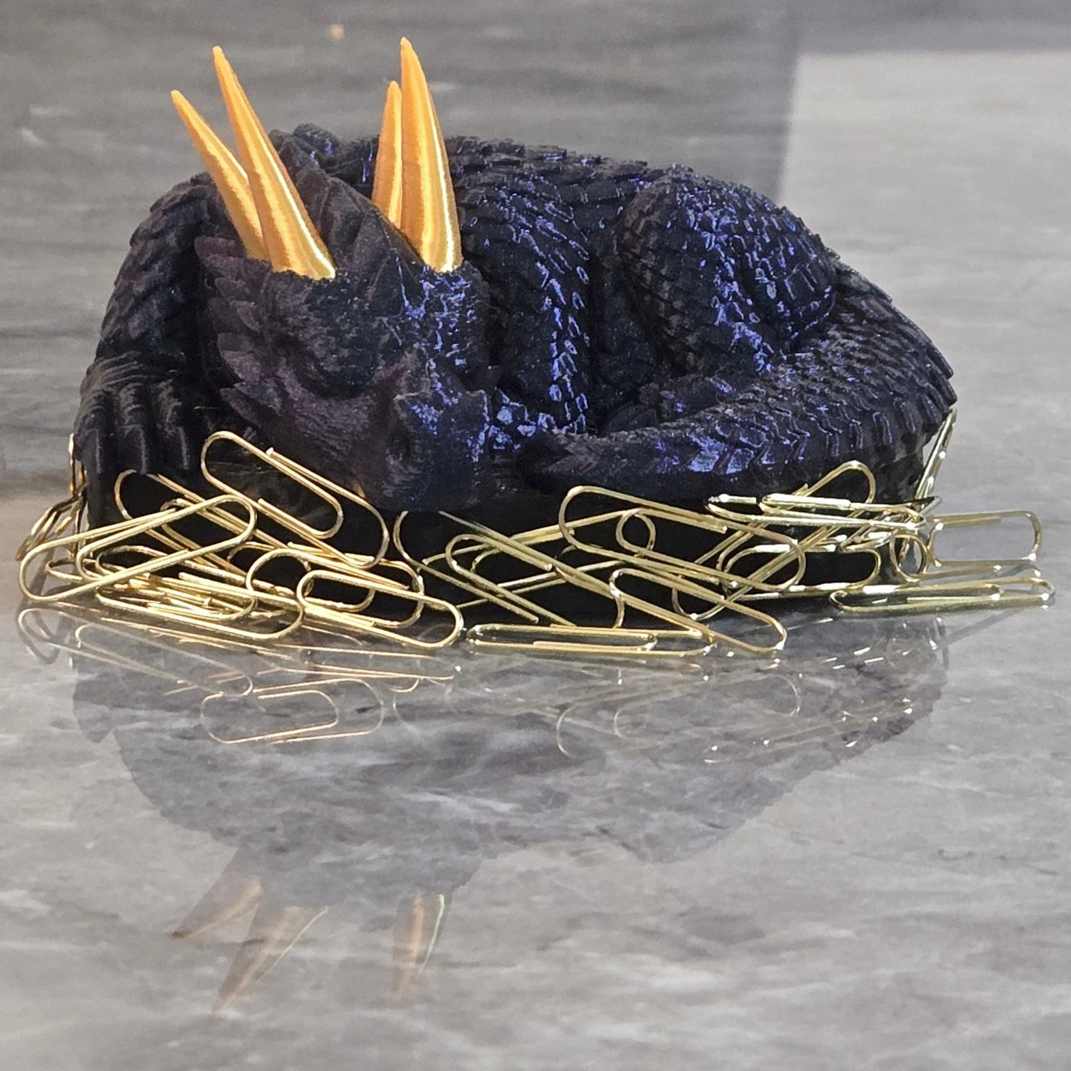 3D printed sleeping dragon in silk blue with gold horns curled in a black nest-shaped base used as a paper clip holder