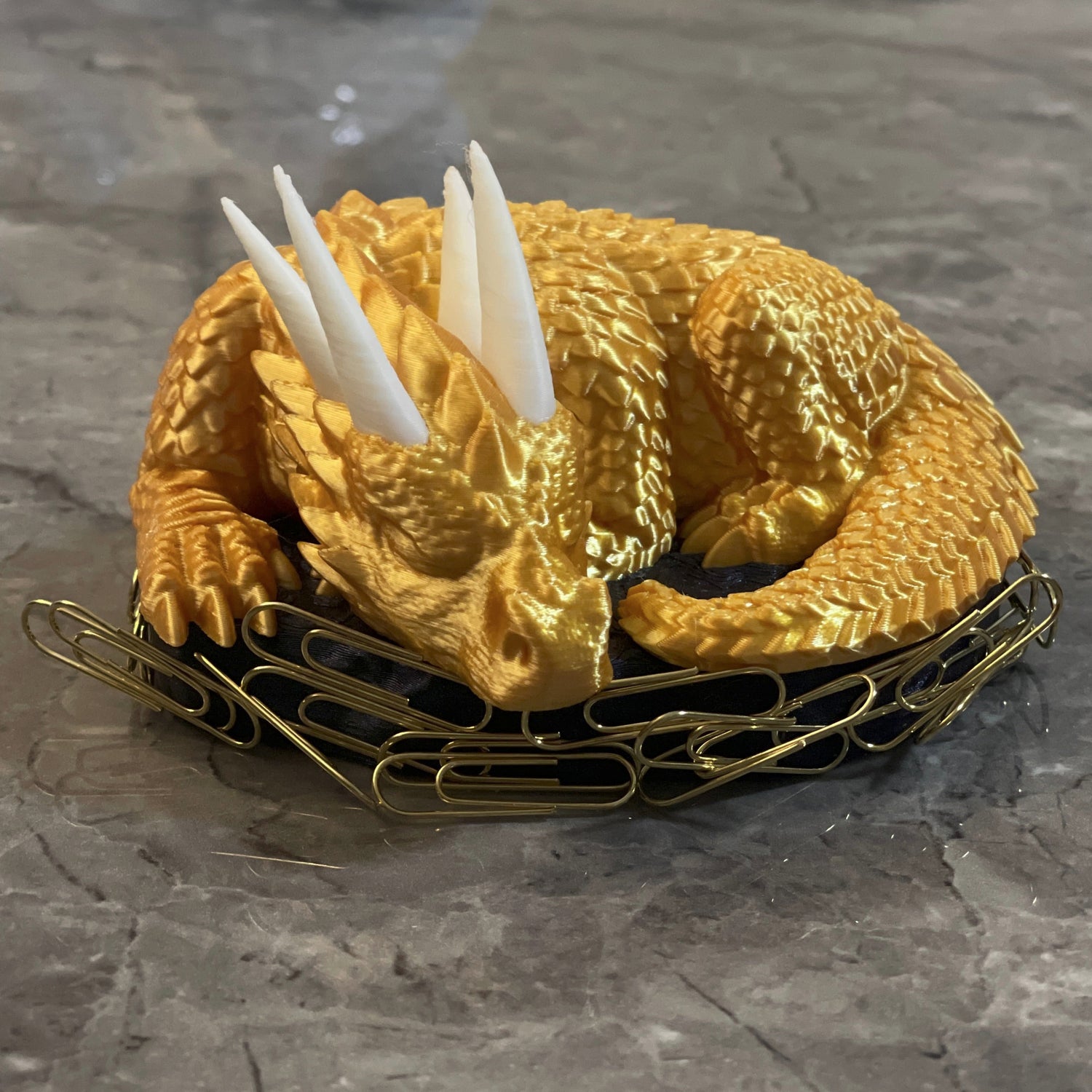 3D printed sleeping dragon in silk Gold with White horns curled in a silk blue nest-shaped base used as a paper clip holder